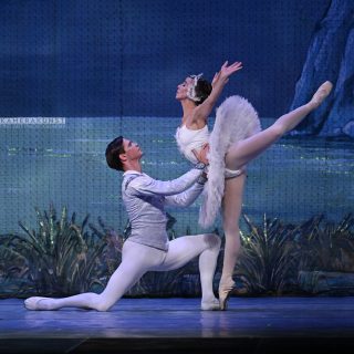 Ballettfotografie: Das Idealbild beim klassischen Ballett: eine zierliche Tänzerin in weißem Tutu, ihr Gesicht von weißen Federn umrahmt, dazu ein anmutiger Prinz.